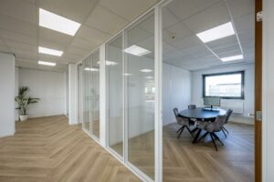 Moderne kantoorruimte aan de Joan Muyskenweg met glazen vergaderruimte, ronde tafel en houten visgraatvloer.